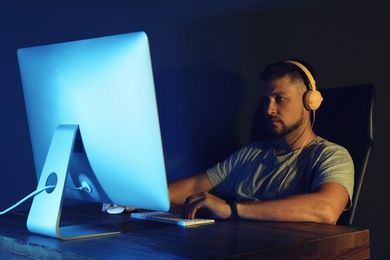 Man with headphones playing video game on modern computer in dark room