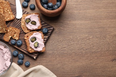 Tasty sandwiches with cream cheese and blueberries on wooden table, flat lay. Space for text