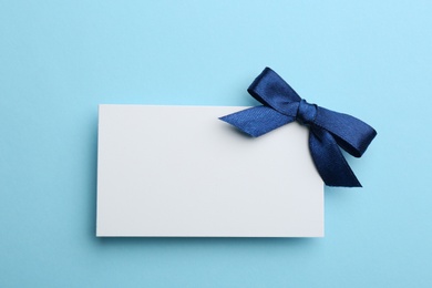 Gift card with bow on light blue background, top view. Mockup for design