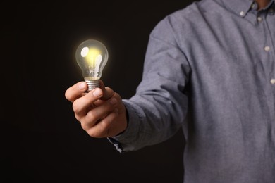 Glow up your ideas. Closeup view of man holding light bulb on black background