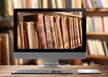 Online library. Modern computer on wooden table and shelves with books indoors