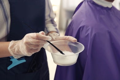 Professional hairdresser holding bowl with hair dye in beauty salon, closeup