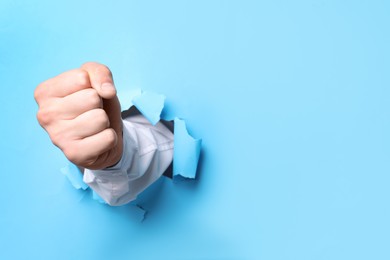 Businessman breaking through light blue paper with fist, closeup. Space for text