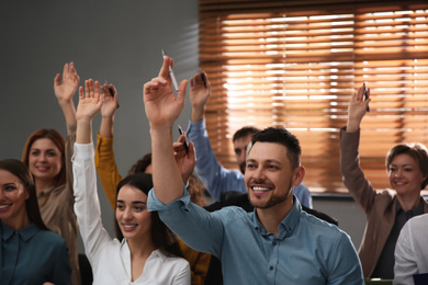 People raising hands to ask questions at seminar in office
