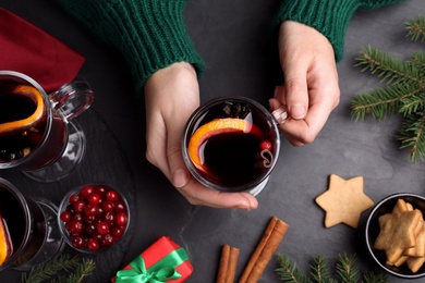 Woman with cup of aromatic mulled wine at black table, top view
