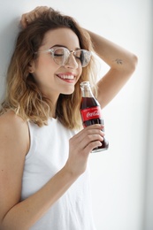 MYKOLAIV, UKRAINE - NOVEMBER 28, 2018: Young woman with bottle of Coca-Cola indoors