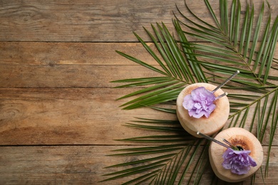 Fresh coconuts with drinking straws and flowers on wooden table, flat lay. Space for text