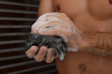 Photo of Man with mesh pouf taking shower at home, closeup