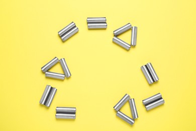 Photo of Recycling symbol made of batteries on yellow background, top view