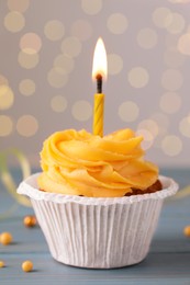 Tasty birthday cupcake on light blue wooden table against blurred lights, closeup