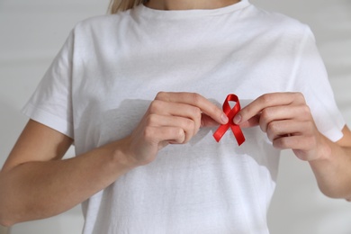 Woman holding red awareness ribbon on light background, closeup. World AIDS disease day