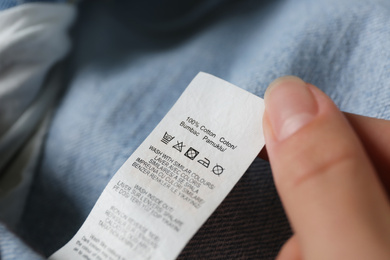 Woman reading clothing label with care symbols and material content on jeans, closeup
