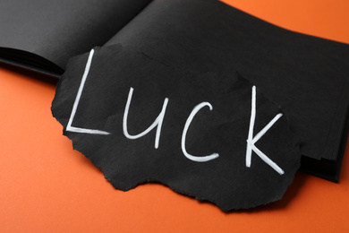Sheet of paper and notebook with word LUCK on orange background, closeup