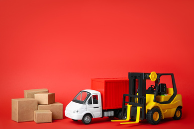 Different toy vehicles with boxes on red background. Logistics and wholesale concept