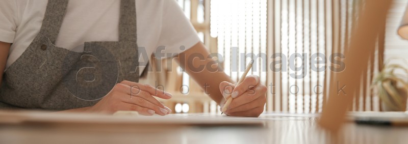 Young woman drawing with pencil at table indoors, closeup. Banner design