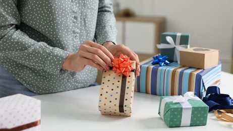 Photo of Woman decorating gift box with bow at white table indoors, closeup