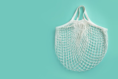 Empty white net bag on turquoise background, top view. Space for text