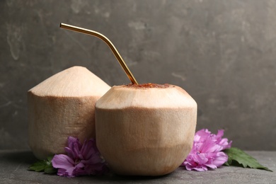 Young peeled coconuts with straw, palm leaf and beautiful flower on grey table