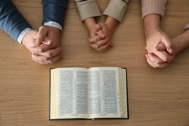 Boy and his godparents praying together at wooden table, top view