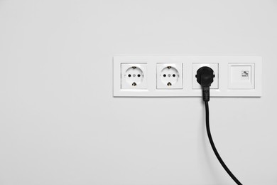 Power sockets with inserted plug on white wall, space for text. Electrical supply