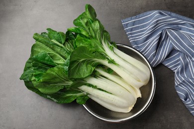 Fresh green pak choy cabbages with water drops in sieve on grey table, top view