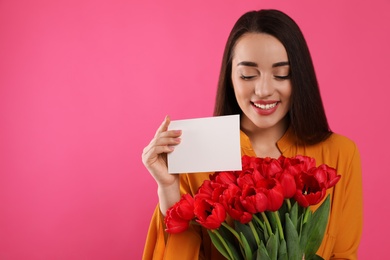 Happy woman with red tulip bouquet and greeting card on pink background, space for text. 8th of March celebration