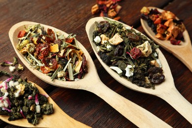 Photo of Spoons with dried herbal tea leaves on wooden table, closeup