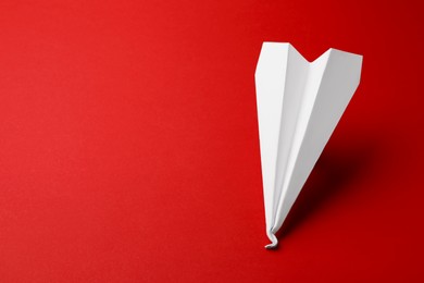Photo of Handmade white paper plane on red background, space for text