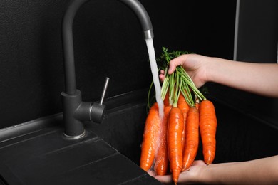 Woman washing fresh ripe juicy carrots under tap water in sink, closeup