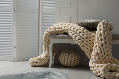 Photo of Indoor bench with soft chunky knit blanket, cushion and pouf in room. Interior design