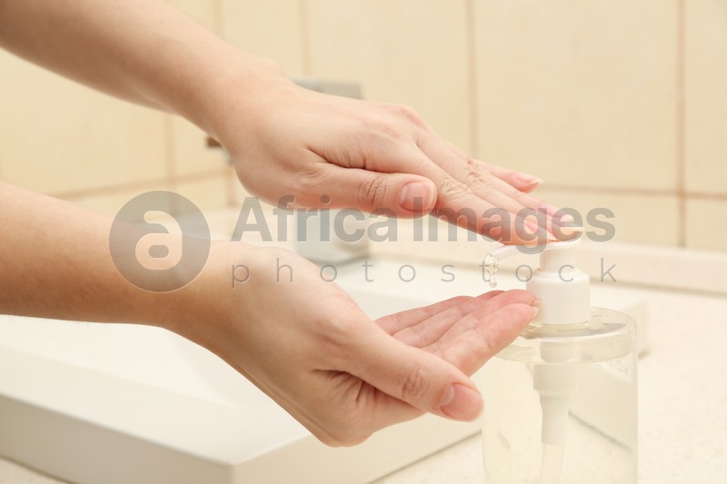 Woman applying antiseptic gel on hand in public bathroom, closeup