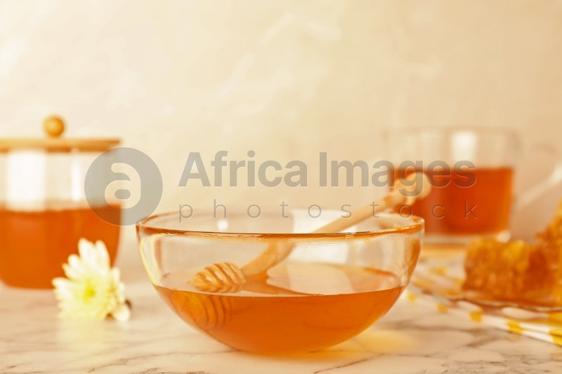 Photo of Glass bowl with tasty honey and dipper on marble table