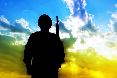 Stop war in Ukraine. Silhouette of armed soldier against sky in Ukrainian flag colors