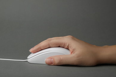 Woman using wired computer mouse on grey background, closeup