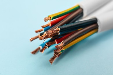 Cables with stripped electrical wires on light blue background, closeup