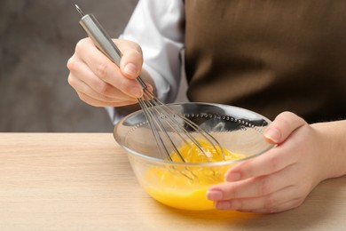 Woman whisking eggs in glass bowl at wooden table, closeup