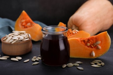 Photo of Fresh pumpkin seed oil in glass jar on dark grey table