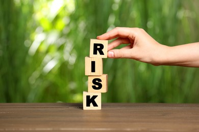 Woman stacking cubes with word Risk on wooden table, closeup