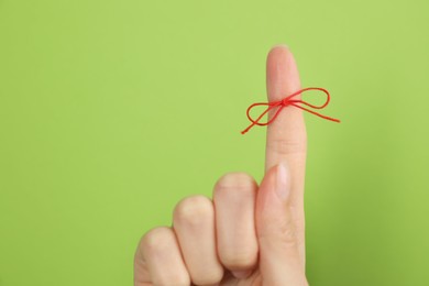 Woman showing index finger with tied red bow as reminder on light green background, closeup