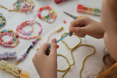 Girl making beaded jewelry at white wooden table, closeup