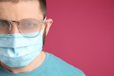 Man with foggy glasses caused by wearing disposable mask on pink background, space for text. Protective measure during coronavirus pandemic