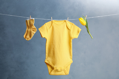 Child's bodysuit, pair of socks and flower hanging on laundry line against dark background