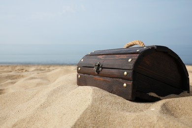 Photo of Closed wooden treasure chest on sandy beach, space for text