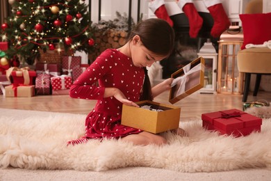 Cute child opening Christmas gift on floor at home