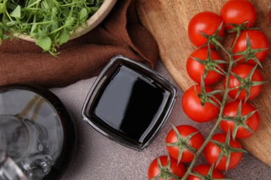 Photo of Organic balsamic vinegar, tomatoes and greens on grey table, flat lay