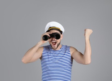 Happy sailor looking through binoculars on grey background