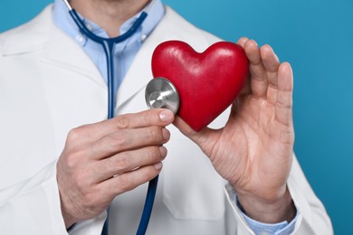 Doctor with stethoscope and red heart on light blue background, closeup. Cardiology concept
