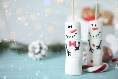 Funny snowmen made of marshmallows on light blue wooden table, closeup. Space for text