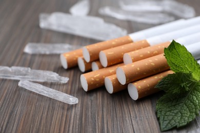 Cigarettes, menthol crystals and mint on wooden table, closeup
