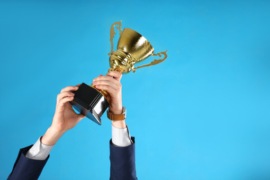 Businessman holding gold trophy cup on light blue background, closeup. Space for text